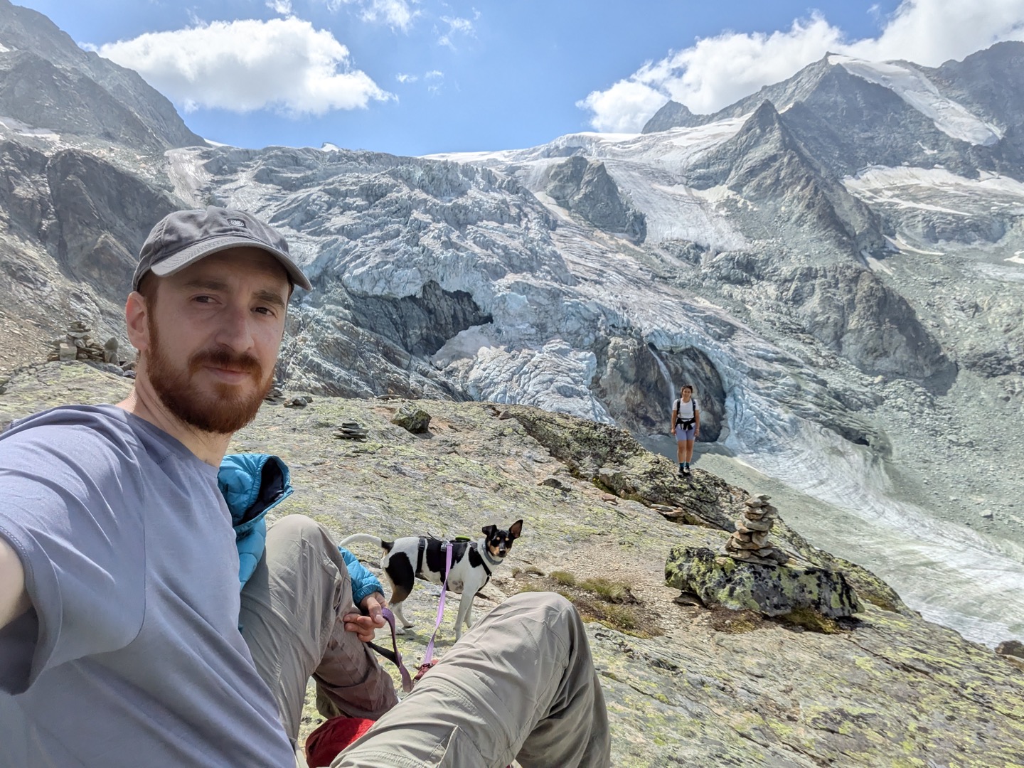 Miguel with his dog Gilda in the foreground and his partner standing on a rock outcrop, with a glacier behind them